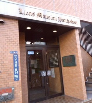 ライオンズマンション八丁堀エントランス (2)｜エントランスは、ガラスドアとレトロな銘板が印象的で、1980年代らしい雰囲気を保ちながらも清掃が行き届いています。