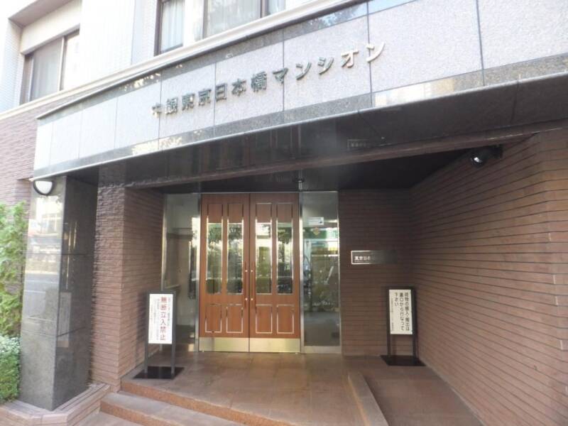 中銀東京日本橋マンシオン エントランス｜重厚感のある木製ドアとグレーの石造りの庇がクラシカルな印象。建物名のロゴサインが高級感を引き立てています。
