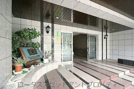 ライオンズマンション門前仲町琴平エントランス｜エントランスは、石貼りの床とガラス扉が設けられ、植栽と銘板が住戸の顔として整えられています。段差にはスロープが付き、バリアフリーにも配慮されています。
