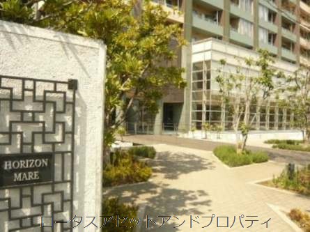 オリゾンマーレエントランス｜敷地内の植栽と石畳のアプローチが整備され、自然と調和した落ち着いた空間が広がっています。エントランスはガラス張りで、外観にも高級感が感じられます。