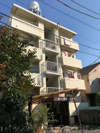 ルーラルハイツの外観。ベージュ系のタイル貼りと白い外壁のコントラストが特徴的な4階建ての低層フォルム。落ち着いた住宅街に馴染むシンプルな設計で、共用階段や植栽も整備され、清潔感のある印象を与えます。
