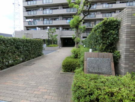 ファミール亀有弐番館外観共用部3｜エントランス部のアプローチはすっと引きのある長めのアプローチです。植栽も適切に管理され、石造りの館銘板が目を引く、高級感を感じるタイプです。
