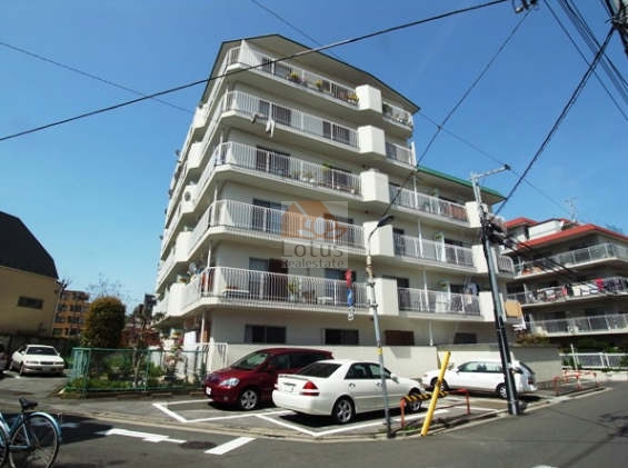 西赤羽グリーンハイツの北東角から撮影した外観。白い外壁と横ラインのバルコニー手すりが整った印象を与える。敷地外周にゆとりがあり、角地立地で開放感がある。西赤羽グリーンハイツは、昭和52年築、6階建てのマンションです。