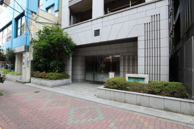日神デュオステージ浅草三筋エントランス1｜石貼りの外壁に植栽が施され、マンション前面には段差の少ないアプローチが整えられています。ガラス扉と庇のある構造で、防犯性と利便性に配慮された設計です。