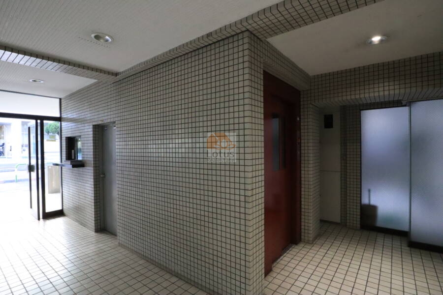 朝日小日向マンション共用部1｜エントランスホールはタイル貼りで統一され、天井の照明が明るく安全な雰囲気を保っています。エレベーターと管理窓口が近接し、動線もスムーズです。