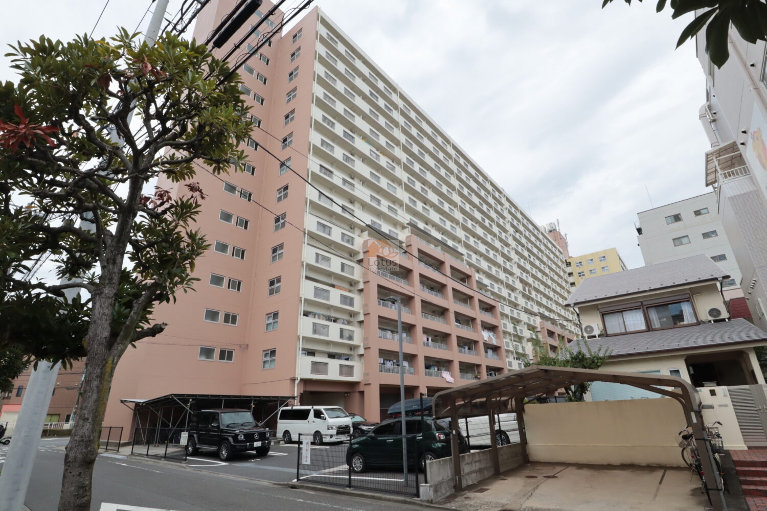 葛西住宅マンションの東側外観という位置づけです。淡いピンクと白の外壁が連続し、横に長い住棟構成が一目で伝わります。敷地前面には駐車スペースが整理され、生活動線と車両動線が分けて計画されている様子が現在進行形で感じられます。