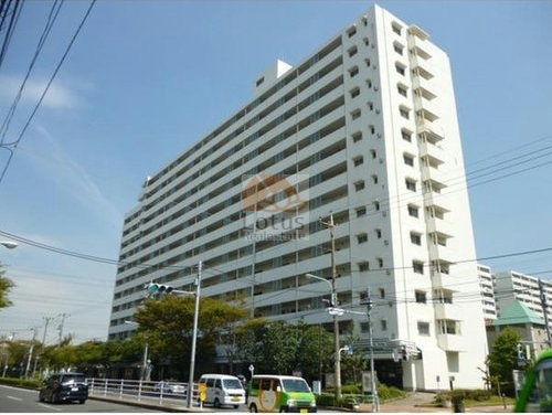 白を基調とした大規模マンションの外観です。地上14階建ての住棟が並び、整備された街路樹と歩道に面して建っています。