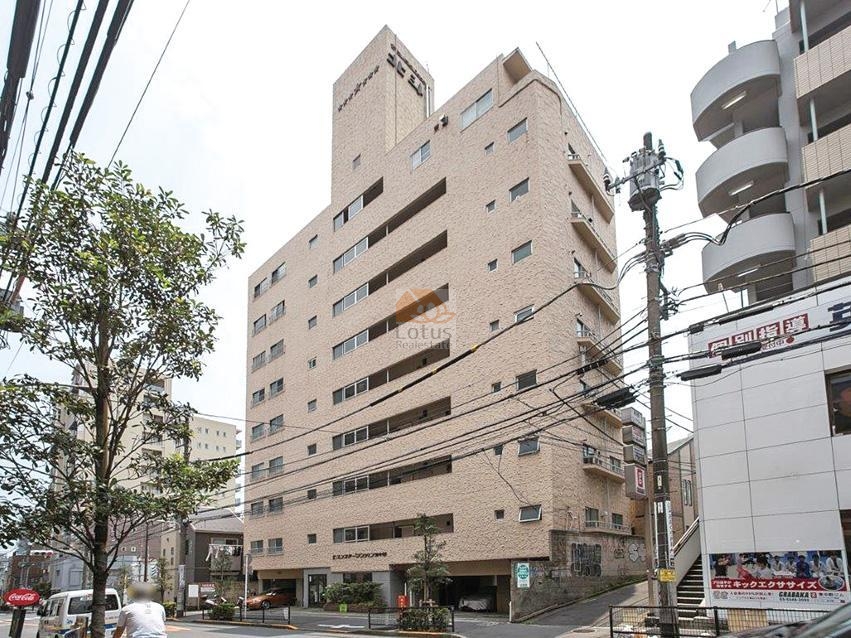 セブンスターマンション東中野の外観。淡い色調の外壁が連続する地上9階建の外観は、周辺の街並みに落ち着きを与えながらも存在感を放っています。道路沿いに整えられた植栽が、都市の喧騒を和らげる入口の前景として機能しています。セブンスターマンション東中野は、昭和45年築、9階建てのマンションです。