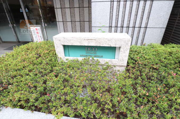 日神デュオステージ浅草三筋エントランス｜植栽の中に設けられた石造りの銘板には、DUO STAGE ASAKUSA MISUGIの文字が刻まれています。正面エントランス左手に配置され、訪問者に建物名をしっかりと伝えます。