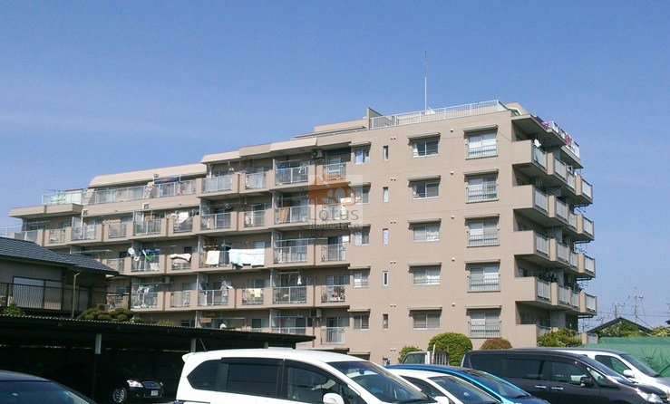 ベージュ系の外壁、前面には駐車場があり、屋根付きの駐車スペースと植栽が配置されています。竹の塚ハイツは、昭和59築、7階建てのマンションです。