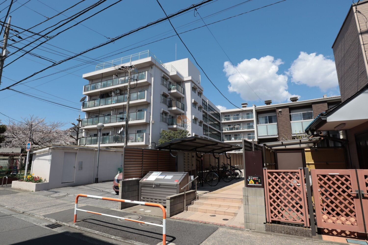 竹の塚ビューハイツの外観。道路に面した棟で、ガラス手すりのバルコニーが縦方向にそろった5階建の中層フラット型です。前面には駐輪場とゴミ置き場があり、生活動線が建物手前で完結しやすい構成になっています。周辺は第一種中高層住居専用地域で、車通りの少ない住宅街といえます。竹の塚ビューハイツは、昭和４９年築、5階建てのマンションです。