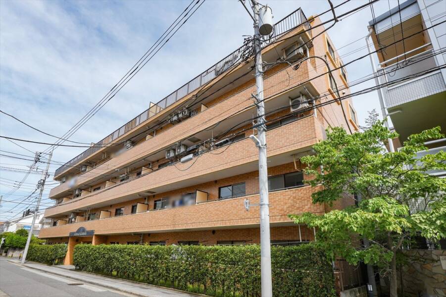 ダイアパレス北綾瀬Ⅱの外観：タイル貼りの外壁とバルコニーのガラス手すりが整然と配置された5階建ての建物です。道路沿いの低層住宅地に建ち、落ち着いた住宅街の雰囲気が感じられます。