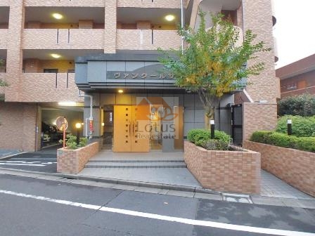 ヴァンクールサウス葛西エントランス１｜植栽に囲まれたアプローチと明るい色味の木製ドアが住まいの印象を引き立てています。