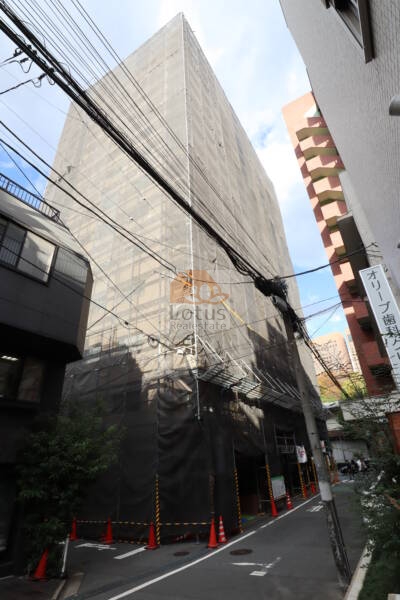新宿パークサイド永谷の外観：十三社通りに面した13階建ての建物で、直線的なバルコニーラインが特徴です。目の前には熊野神社の木々が広がり、都市の中に自然を感じられる立地です。