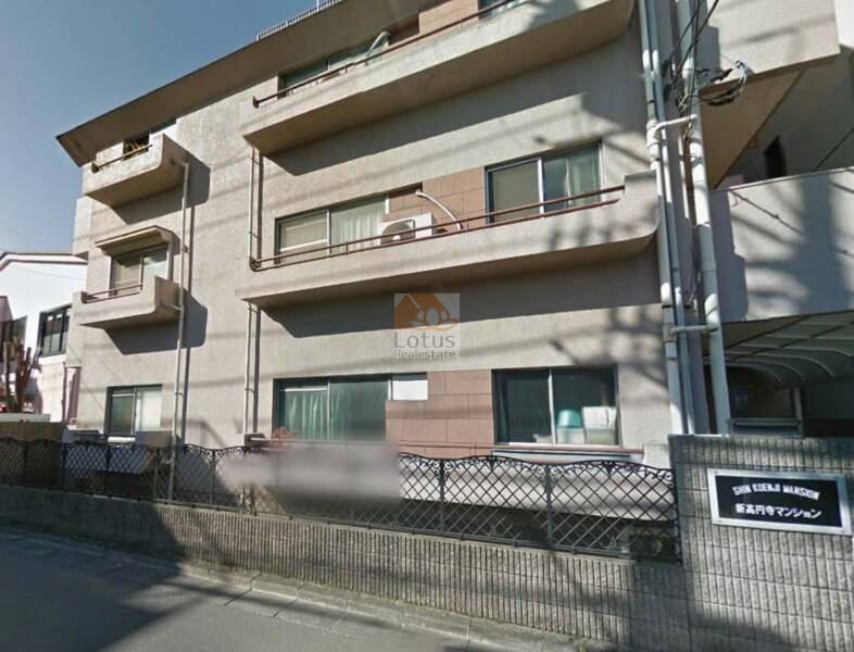 新高円寺マンションの外観は、横長の庇とベージュ系タイルを基調とした落ち着いた佇まいが特徴です。低層の戸建てが混在する静かな住宅街に位置し、ファサードの一部に茶色のアクセントパネルが設けられています。