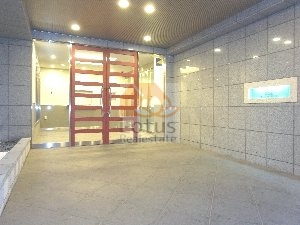 日神デュオステージ浅草今戸エントランス｜石調タイルに囲まれたエントランス空間には、ガラス張りのドアと赤い縦格子のデザイン扉が設置されている。照明付きで夜間も視認性が高く、防犯性にも配慮された設計です。