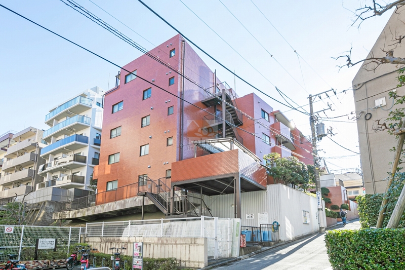 マンション小石川の外観（北西側より撮影）。傾斜地を活かした設計で、建物下部には鉄骨による持ち上げ構造が採用されている。周囲には中高層の住宅が並び、落ち着いた住宅街に溶け込むロケーション。マンション小石川は、昭和55年築、5階建てのマンションです。