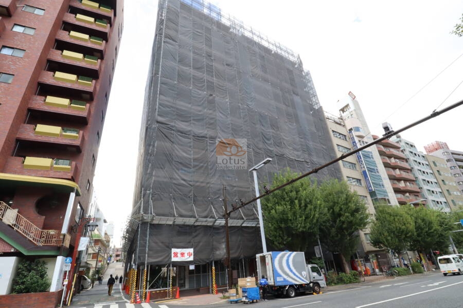 新宿パークサイド永谷の外観：建物全体が斜めから写され、1階部分の店舗区画や歩道との距離感が分かります。通り沿いで視認性が高く、利便性の良い立地です。