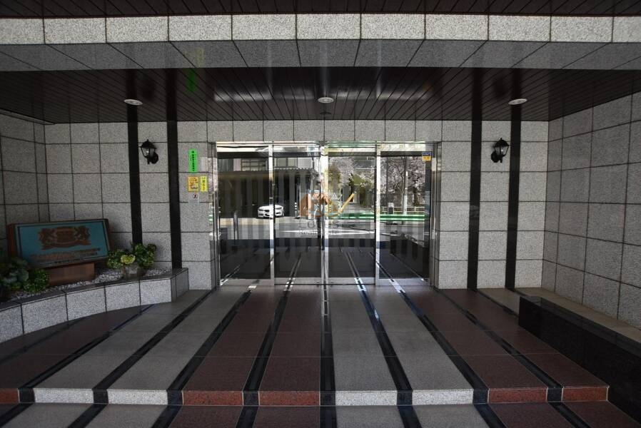 ライオンズマンション門前仲町琴平エントランス１｜エントランス正面は、格子状の天井と石調タイルを組み合わせた造りで、直線的でシャープな印象です。ガラス扉の奥にはオートロック設備が確認できます。