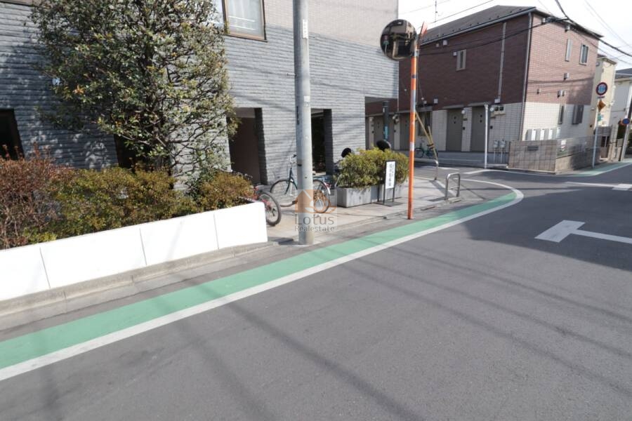 ヴィルヌーブ鷺宮エントランス3｜エントランス前の植栽と自転車スペースが整理されていて、暮らしやすさと穏やかさを感じさせます。角地に位置するため視認性も高く、安心感ある生活の拠点となっています。
