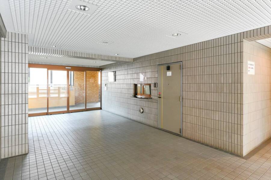 ダイアパレス北綾瀬Ⅱの共用部：管理人室と風除室の空間が写っており、床はタイル張りで清潔に保たれています。管理が行き届いた共用スペースが快適な暮らしを支えます。