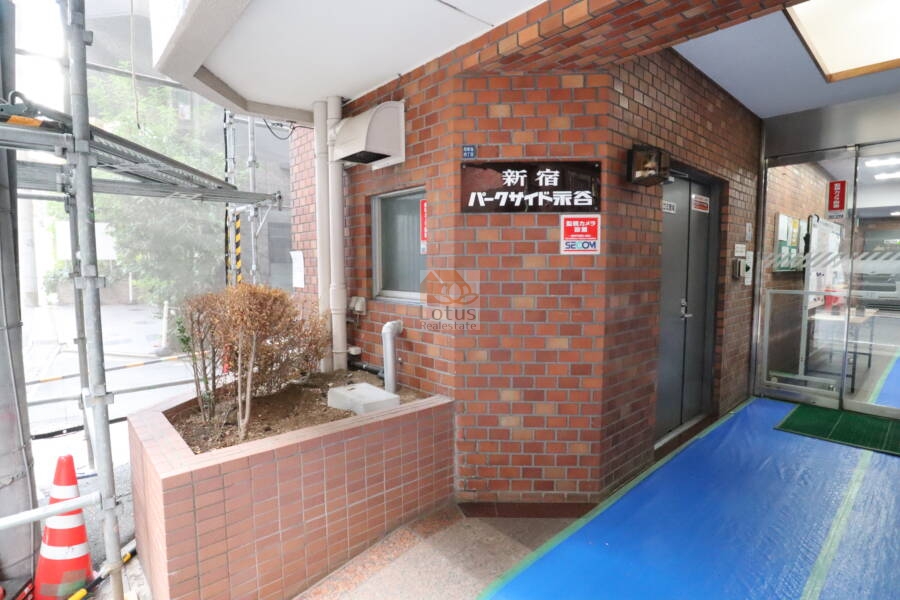 新宿パークサイド永谷のエントランス：夜間の自動ドア付近が写っており、照明の設置が確認できます。防犯面にも配慮された設計です。