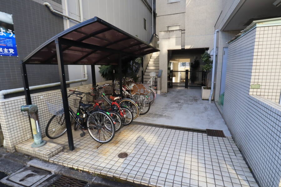 朝日小日向マンション共用部3｜屋根付きの自転車置き場が設けられており、雨天でも安心して利用できます。共用部の導線も明快で、敷地の有効活用が図られています。
