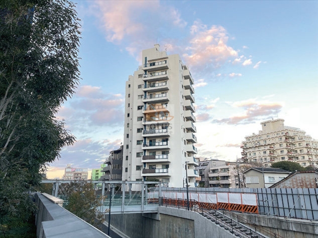中野パークハウスの北側から見た外観。白を基調とした12階建ての縦長フォルムが空に映える、高層感ある佇まい。中野駅徒歩2分の駅近立地でありながら、周囲は抜け感のある開放的な環境。中野パークハウスは、昭和46年築、12階建てのマンションです。