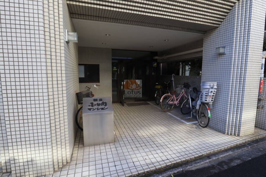 朝日小日向マンションエントランス1｜白いタイル敷きのアプローチが建物と統一され、手入れの行き届いた共用空間を演出しています。マンション名のプレートがしっかりと設置されています。