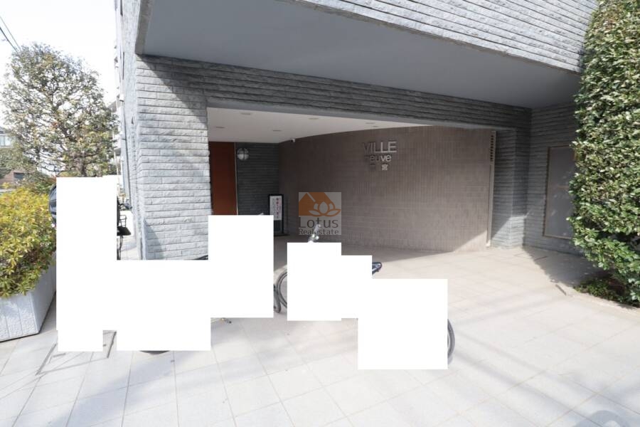 ヴィルヌーブ鷺宮エントランス1｜アプローチは屋根付きで、雨の日も足元が守られます。石調の外壁と植栽のコントラストが、落ち着いた住まいの顔をつくり出しています。
