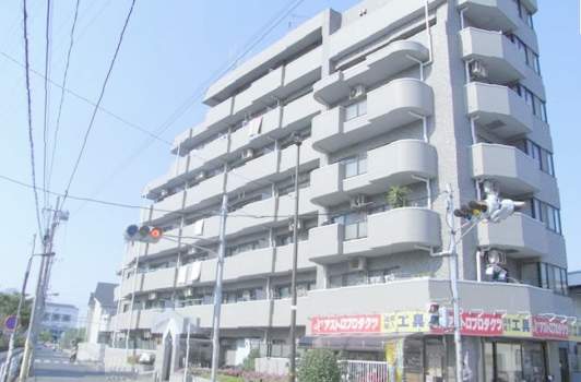 ライオンズマンション竹の塚東の外観。交差点に面した南西角地に建ち、明るいグレー系タイルが日差しに映えています。低層部にはテナントが入り、暮らしの中にちょっとした便利さがプラスされています。