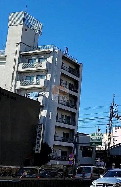 代田橋ハイムの外観を南西側から望んだ構図で、白を基調とした外壁が青空に映えています。角地に立地し、全戸角部屋の設計が視覚的にも伝わるファサードです。代田橋ハイムは、昭和４９年築、７階建てのマンションです。