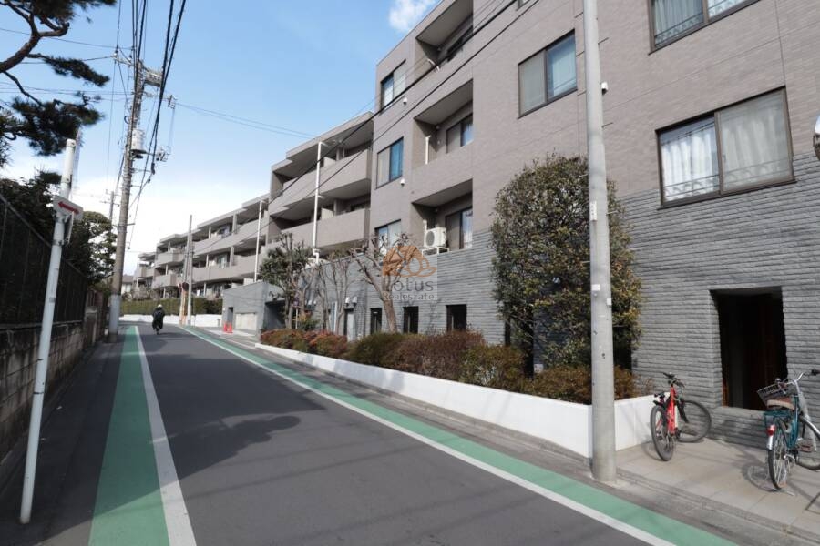 ヴィルヌーブ鷺宮外観22｜並木と植栽に彩られたファサード沿いを歩くたびに、このマンションの丁寧な管理ぶりが感じられます。道沿いの自転車も整然と並び、住まいの落ち着いた暮らしぶりを物語っています。