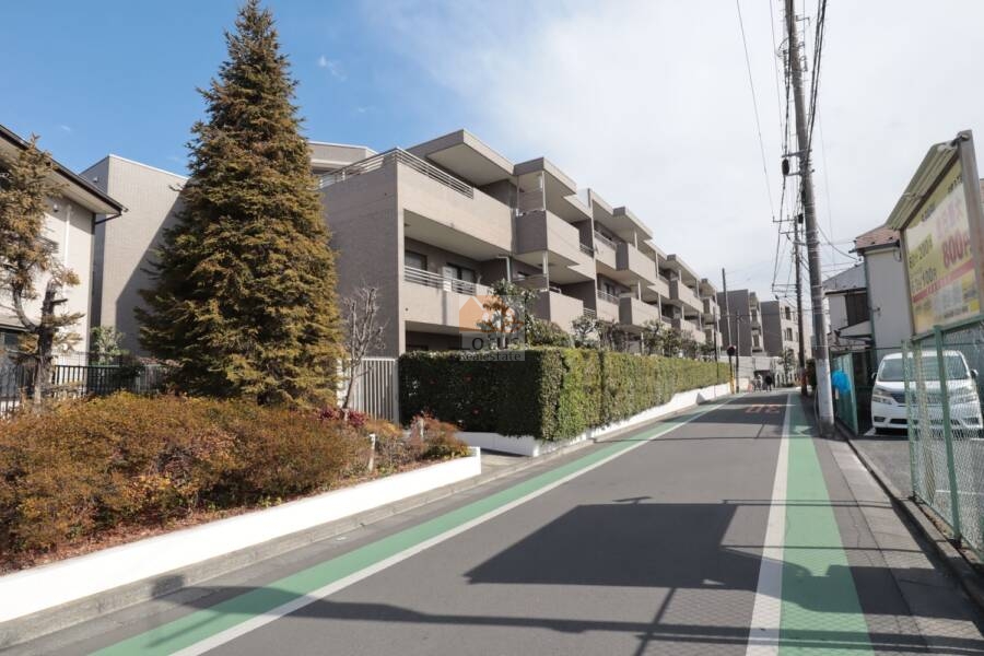ヴィルヌーブ鷺宮外観55｜幅広の歩道と共に続くバルコニーライン。生活導線と景観配慮のバランスが見事です。敷地を取り囲む植栽と外構の白い縁取りが、建物の印象を引き締めています。