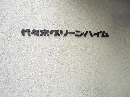 代々木グリーンハイムエントランス2｜代々木グリーンハイムの館銘板。エントランス脇に設置された黒地のプレートに白文字で建物名が表示されている。上品な印象を添えるアクセント。
