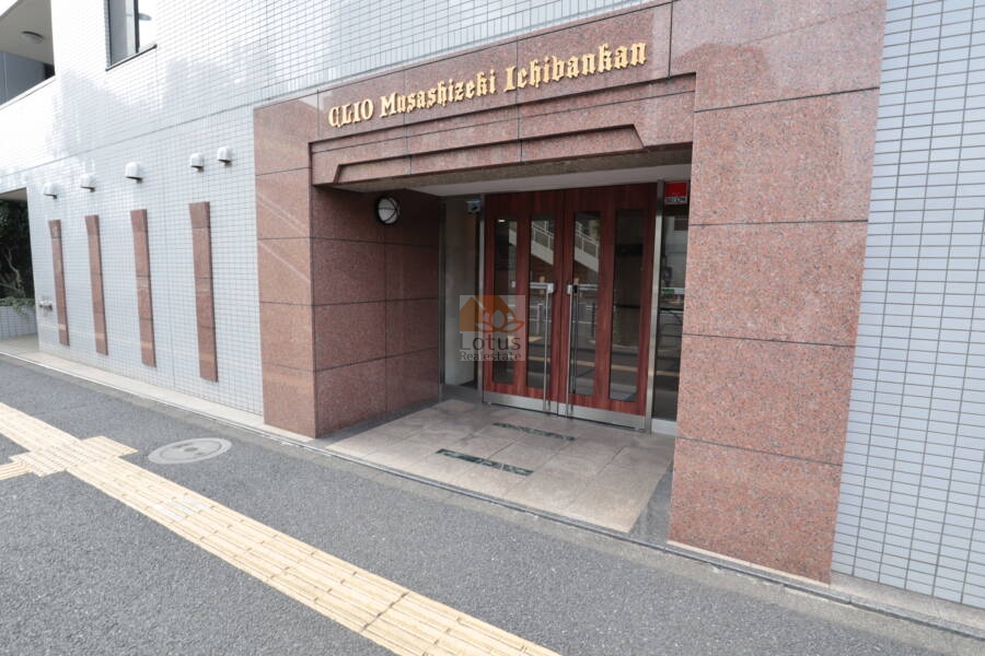 クリオ武蔵関壱番館のエントランス：建物名が刻まれた石板サインと植栽が配置されており、訪れる人に安心感を与える構えです。タイル舗装が迎え入れてくれます。
