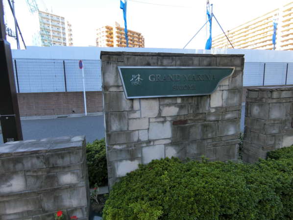 ルネグランマリーナ潮見外観・共用部2｜区道に沿うカタチで細長いアプローチがあります。敷地の東端には館銘板が配置されています。