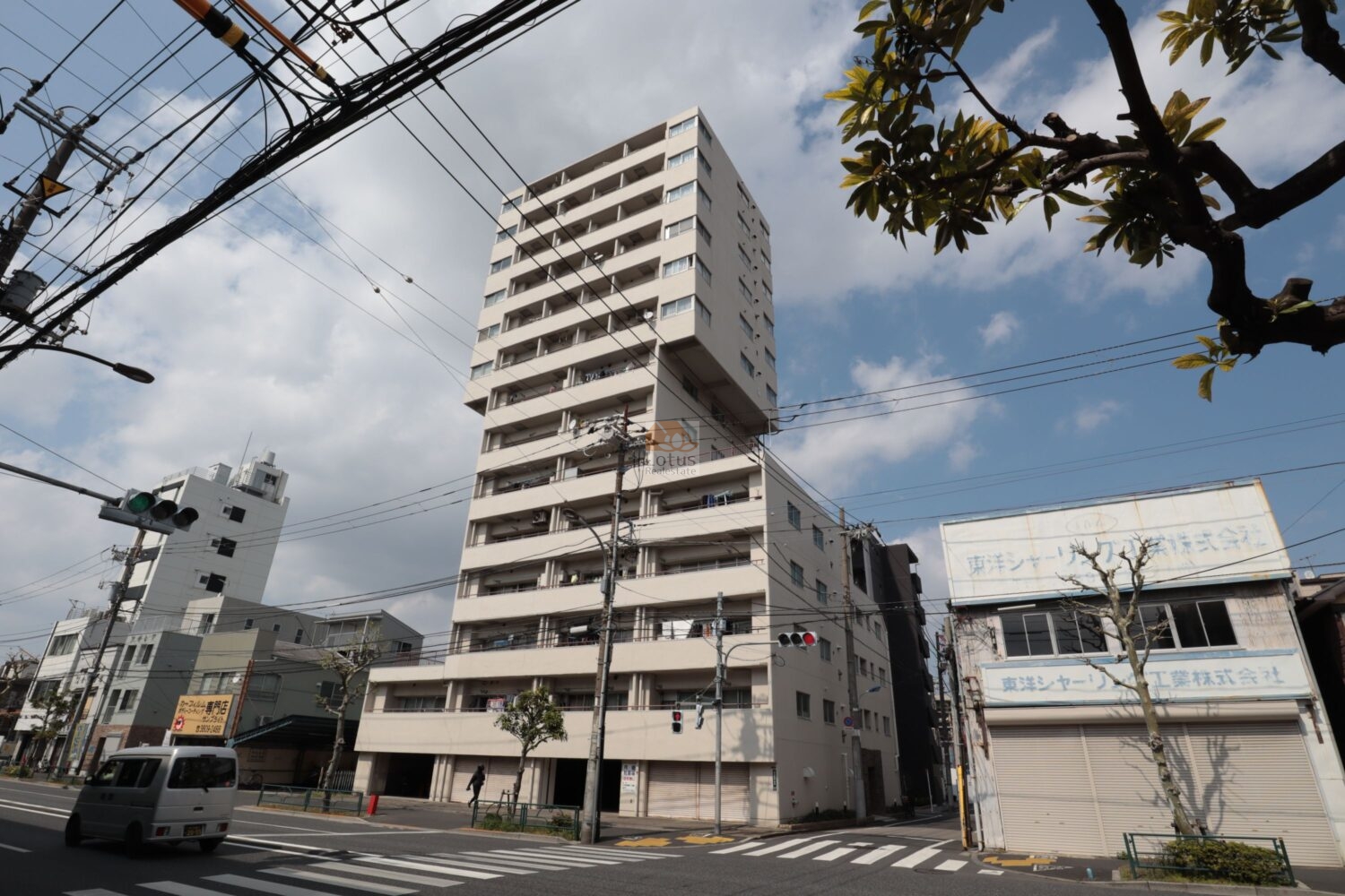青空に白っぽい外壁が映えて、高層14階建てのボリューム感が伝わります。 交差点前の大通りに面しており、街の「顔」として存在感があります。