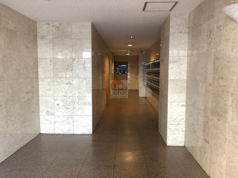 中野東豊マンション共用部４｜光沢のある大理石調のタイルが壁面を覆い、共用廊下は清潔感を保った造りです。片側には集合ポストが整列し、管理の行き届いた印象を与えます。