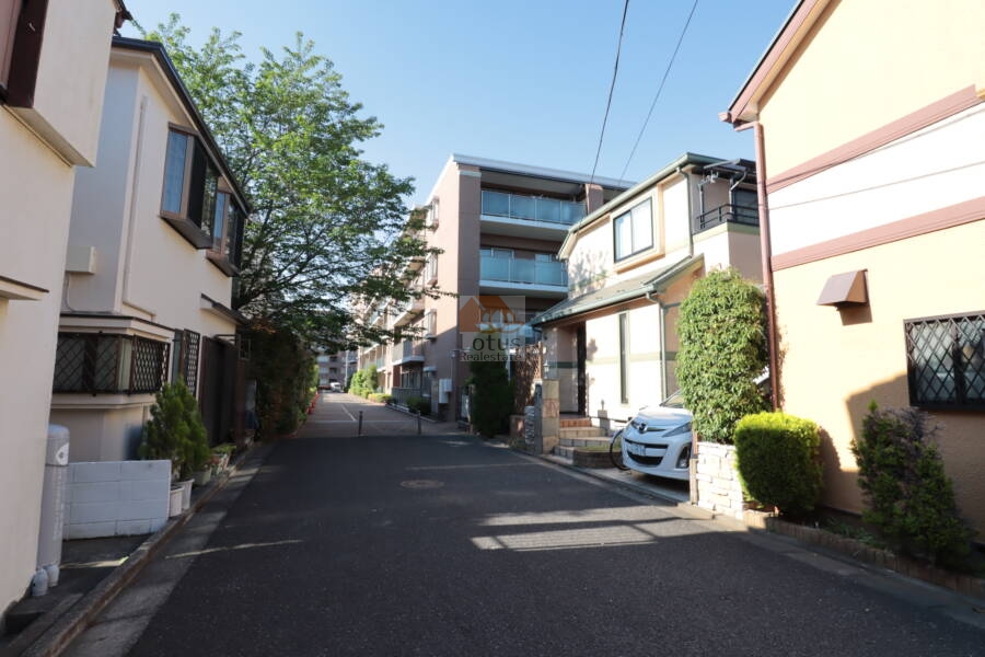 ブロッサムコートむさし野共用部7｜敷地外周には戸建住宅が建ち並ぶ静かな住宅街が広がり、周囲環境との調和が取れた立地。正面にはブラウン系外壁の住棟が控え、周辺との距離感も十分に確保されています。