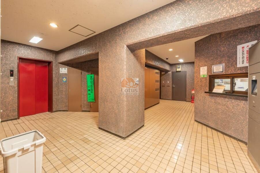 ライオンズマンション護国寺第２エントランスホール｜エントランスホール。赤色のエレベーターが印象的で、郵便受けや掲示板もコンパクトにまとめられています。照明や掲示物が明るく、日常の動線も明確です。