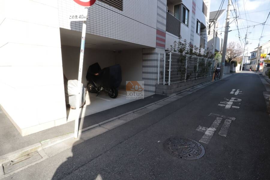 アークス鷺ノ宮共用部2｜奥行きのある屋根付きバイク置場は、大型バイクにも対応する余裕あるレイアウトです。周辺にはフェンスと植栽が施され、防犯面と景観に配慮された共用設計となっています。