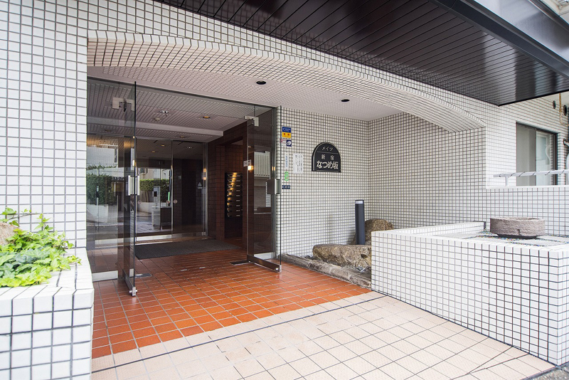 メイツ新宿なつめ坂エントランス２｜ドアの周りは白いタイル、床は赤茶色のタイル張りです。