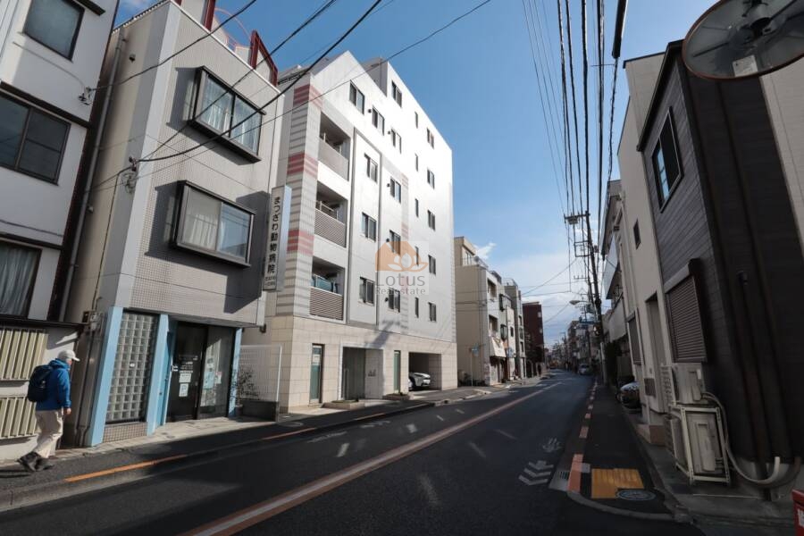 アークス鷺ノ宮外観4｜大通りから見た外観で、低層階の壁面には明るい石調タイルが使われ、上品さを演出しています。バルコニーにはルーバー付きの手すりが採用され、プライバシーにも配慮された設計です。