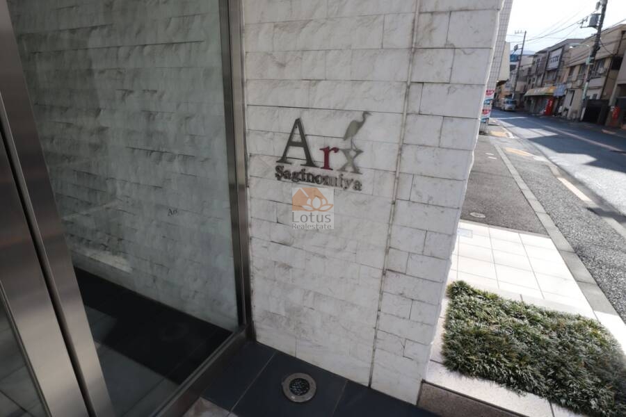 アークス鷺ノ宮エントランス2｜「Arx Saginomiya」のロゴがスタイリッシュに配置された外壁は、デザイン性と認知性を両立。アプローチ部分の植栽が、住まいに柔らかさと品を添えています。