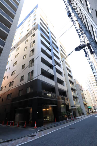 リビオ東京の外観。タイル貼りの黒を基調とした低層部と白を主体とした上層部のコントラストが際立ちます。周囲はオフィスや住宅が混在する街並みで、敷地は前面道路からセットバックして配置されています。リビオ東京は、平成18年築、13階建てのマンションです。