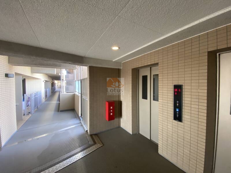 コスモ２１ザガーデンズフォート共用部 (3)｜共用廊下とエレベーターホール。シンプルでありながらも、壁面や床に統一感のあるタイル仕上げが施されています。自然光が差し込む設計で、日中は照明なしでも明るさを確保しています。