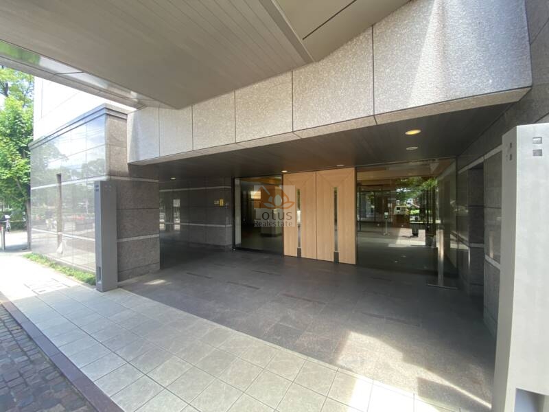 コスモ２１ザガーデンズフォート (6)｜広々とした間口に、左右対称の木調ドアと透明なガラス壁が配置され、整った印象を与えます。風除室の奥には宅配ボックスが設置されており、機能性とデザイン性を両立しています。