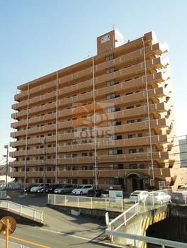 ライオンズマンション北千住第６外観 (2)｜川を挟んだ北面から望むライオンズマンション北千住第６。遠くからでもひときわ目を引く、整ったシルエットが魅力です。背後には電車の高架も見え、交通アクセスの良さも伺えます。