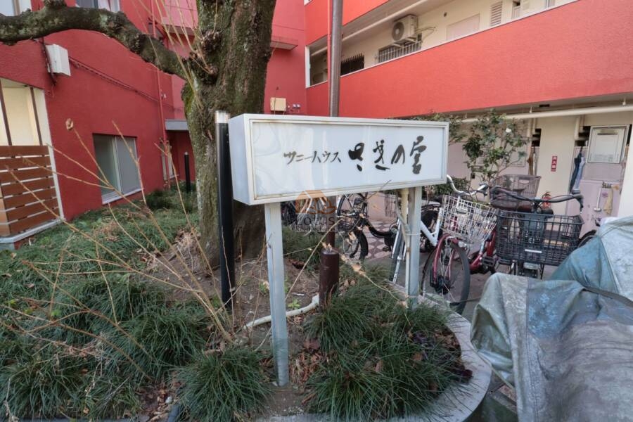 サニーハウスさぎの宮エントランス1｜エントランス前には、自転車が複数台駐輪されており、住民の生活動線として機能しています。タイル貼りの床面や植栽が整備され、落ち着いたアプローチ空間が形成されています。